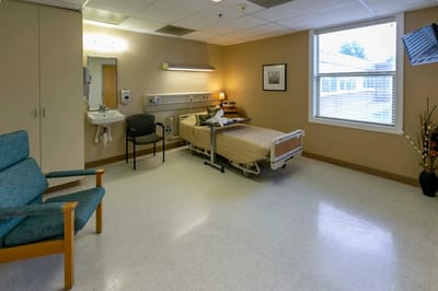 A private room in a senior living facility with a bed and chair