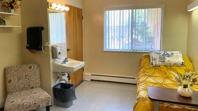 Bright private resident room with a yellow blanket and chair