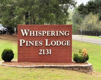 Sign of Whispering Pines Lodge on a sunny day