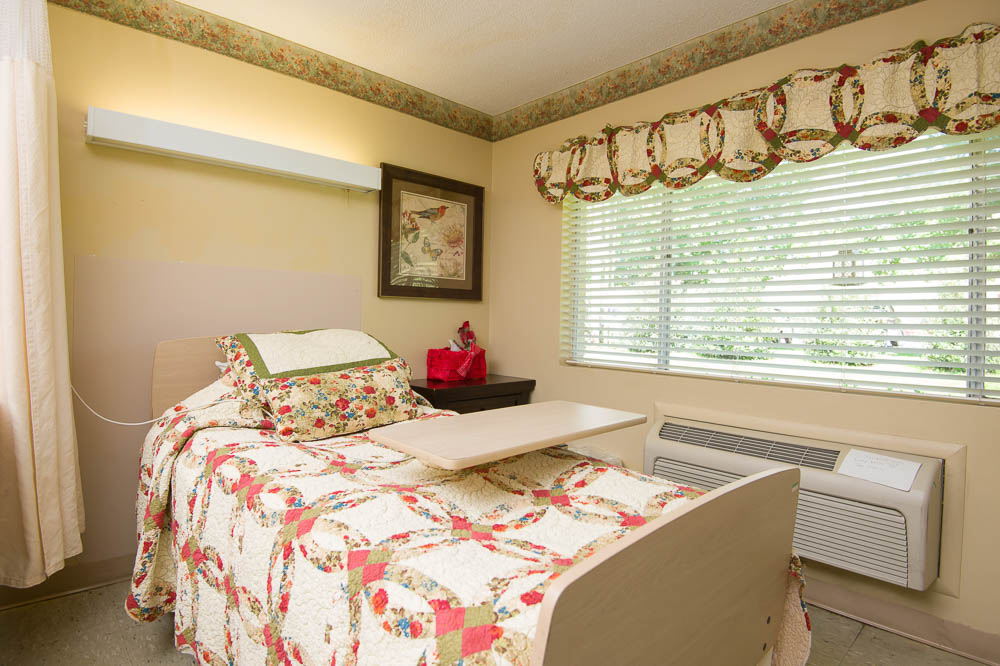 A cozy resident room with a quilted bedspread and window.