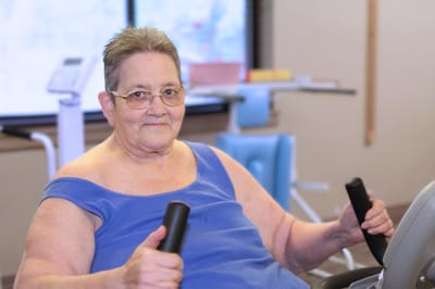 Senior woman using exercise equipment in a fitness area.