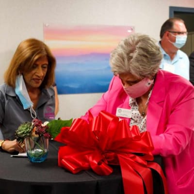 Two women engaged in a ceremony with a large red bow.