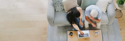 Two individuals interacting over a laptop on a couch.