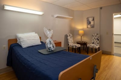 A cozy resident room with a blue bedspread and seating area