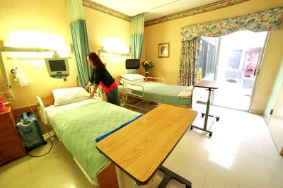 A staff member making a bed in a shared resident room