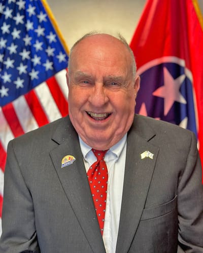 Smiling resident in formal attire with flags behind