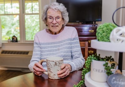 An elderly woman enjoying a beverage indoors.