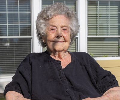 Elderly woman sitting outdoors, smiling.