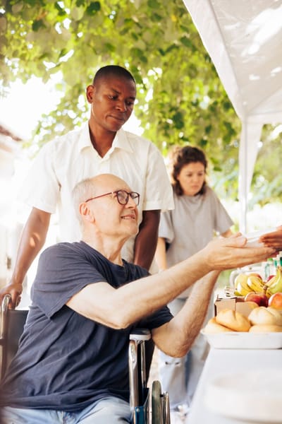 A resident receiving fruit from staff members outdoors