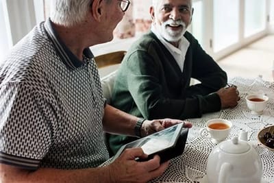 Two seniors enjoying tea and a tablet conversation