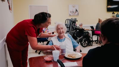 Staff serving food to a smiling resident in a dining area