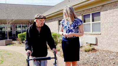 A resident and staff member walking in a garden area