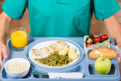 A staff member serving a meal tray with food