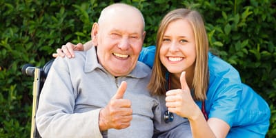 Happy senior resident with caregiver giving thumbs up