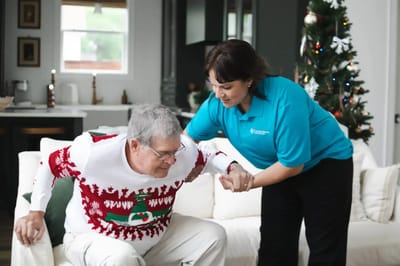 Cornerstone Caregiving – Mobile, home care in Mobile, AL — Senior caregiver assisting man in festive sweater