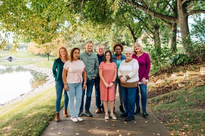 Group of staff members smiling outdoors by a serene pond