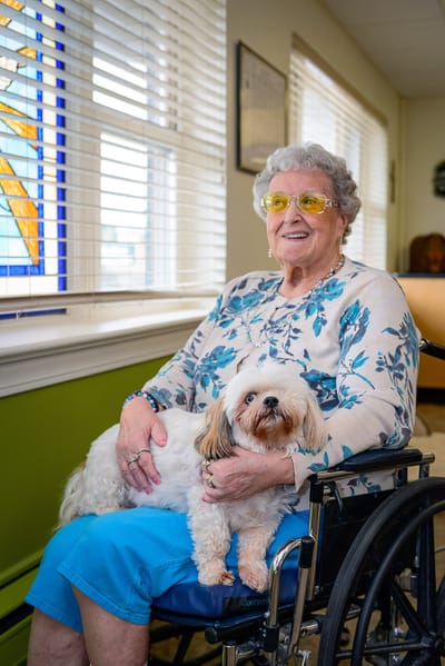 A resident smiling while holding a small dog in a common area
