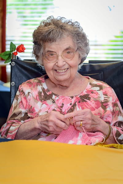 Senior woman smiling while knitting in an activity room