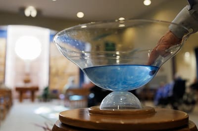 A hand reaching into a decorative bowl of blue water