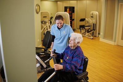 Trainer assisting a senior resident with exercise equipment