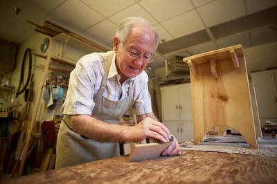 An elderly man sandpapering wood in a workshop