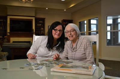 Staff assisting resident with a puzzle in a cozy common area