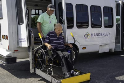 Staff assisting resident from a facility transport van