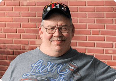 Smiling man wearing a cap in front of brick wall