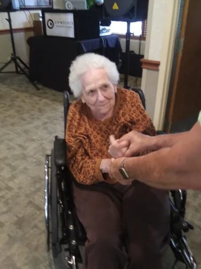 An elderly woman in a wheelchair being assisted