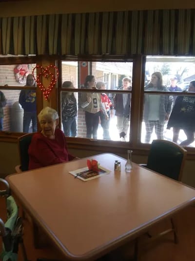 Resident in dining room with visitors outside window