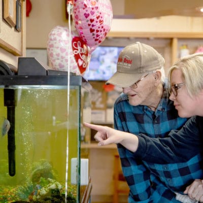 A resident and staff member observing a fish tank together