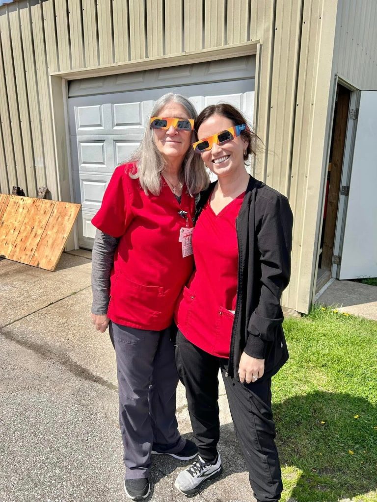 Two staff members posing outside with fun glasses