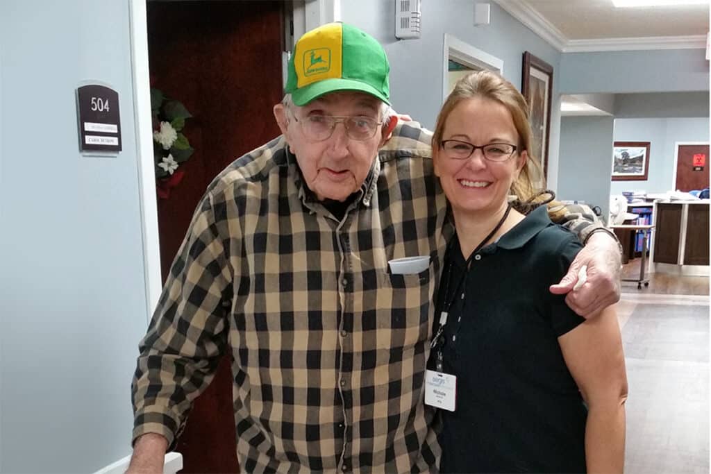 A resident and staff member smiling together in a hallway