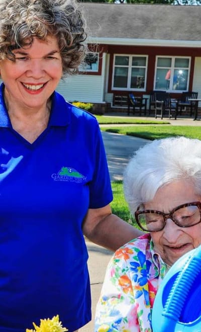 Staff assisting a resident outdoors with flowers