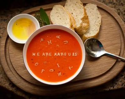 Bowl of soup with letters and bread on a wooden board