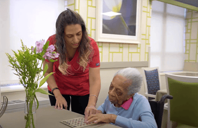 Staff assisting a resident with bingo in a bright activity room