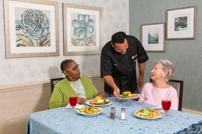 Residents enjoying a meal with attentive staff in a dining area