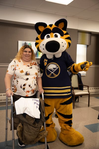 Resident posing with a cheerful mascot in an activity room