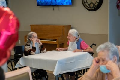 Two elderly women chatting at a table in a common area