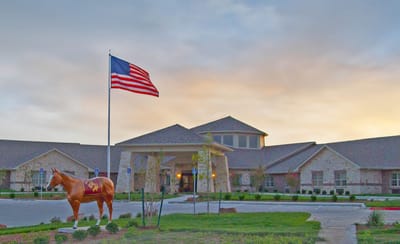 Exterior view of a senior living facility with a flag and horse statue