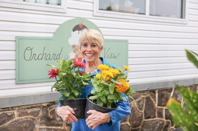 A resident holding potted flowers near the facility sign