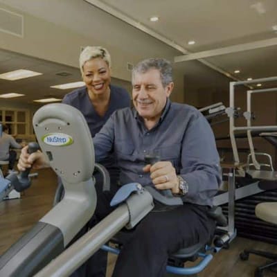 Resident using rehabilitation equipment with staff assistance