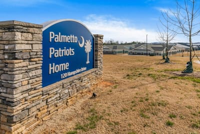 Sign for Palmetto Patriots Home with buildings in background