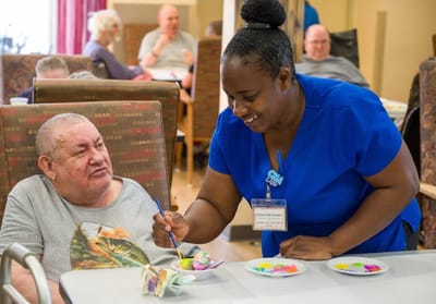 A caregiver assisting a resident with painting activity