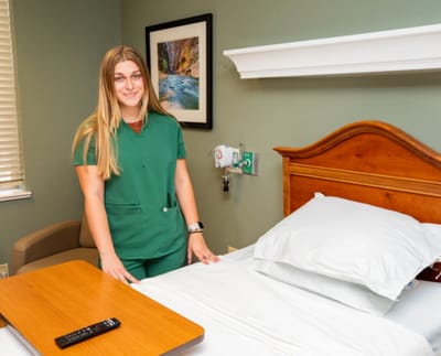 Nurse standing by a neatly made bed in a resident room