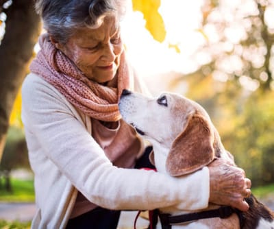 A senior woman smiling while interacting with a dog outdoors