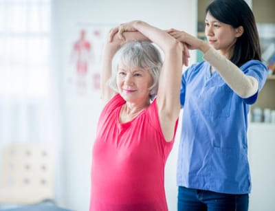 A staff member assisting a senior with stretching exercises