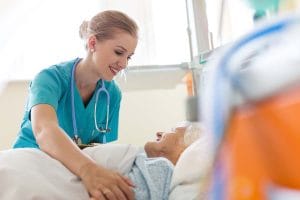 Fort Valley Health and Rehab, Nursing Home in Fort Valley, GA — Nurse assisting a smiling elderly patient in bed