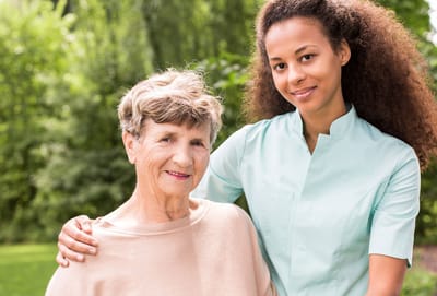 A caregiver poses with a smiling resident outdoors