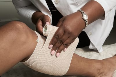 A healthcare worker bandaging a patient's knee
